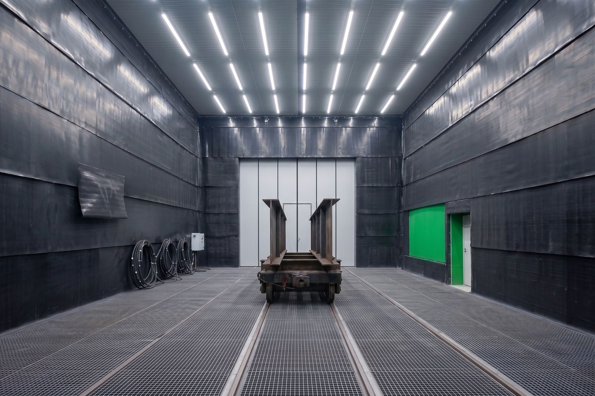 Freistrahlhalle mit Schrapper-Schienenwagen auf Gitterrostboden, Gleise führen zum Tor